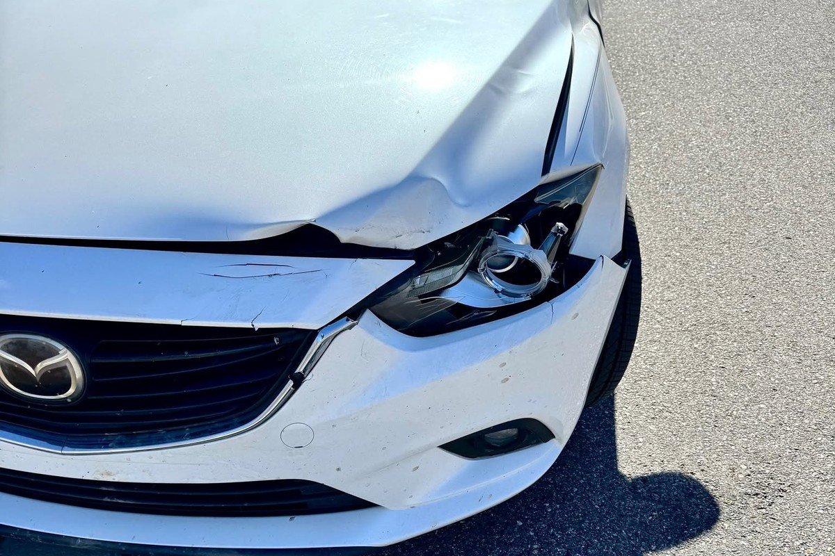 White Mazda sedan with front-end collision damage to the hood, headlight and bumper, before repair at Lankford Paint & Body
