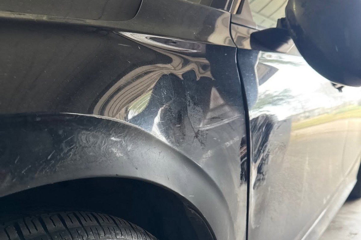 Crease and scraped paint along the front fender and door of a black sedan, before repair at Lankford Paint & Body